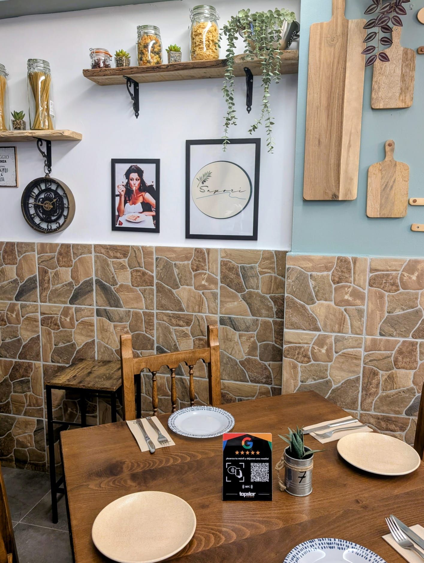 Interior de restaurante con mesa de madera, platos y decoraciones en las paredes.