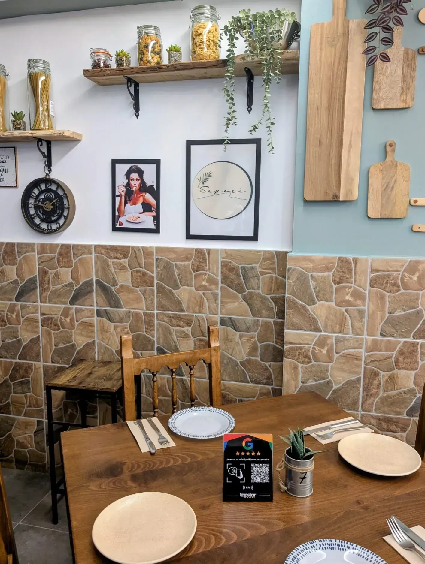Interior de restaurante con mesa de madera, platos y decoraciones en las paredes.