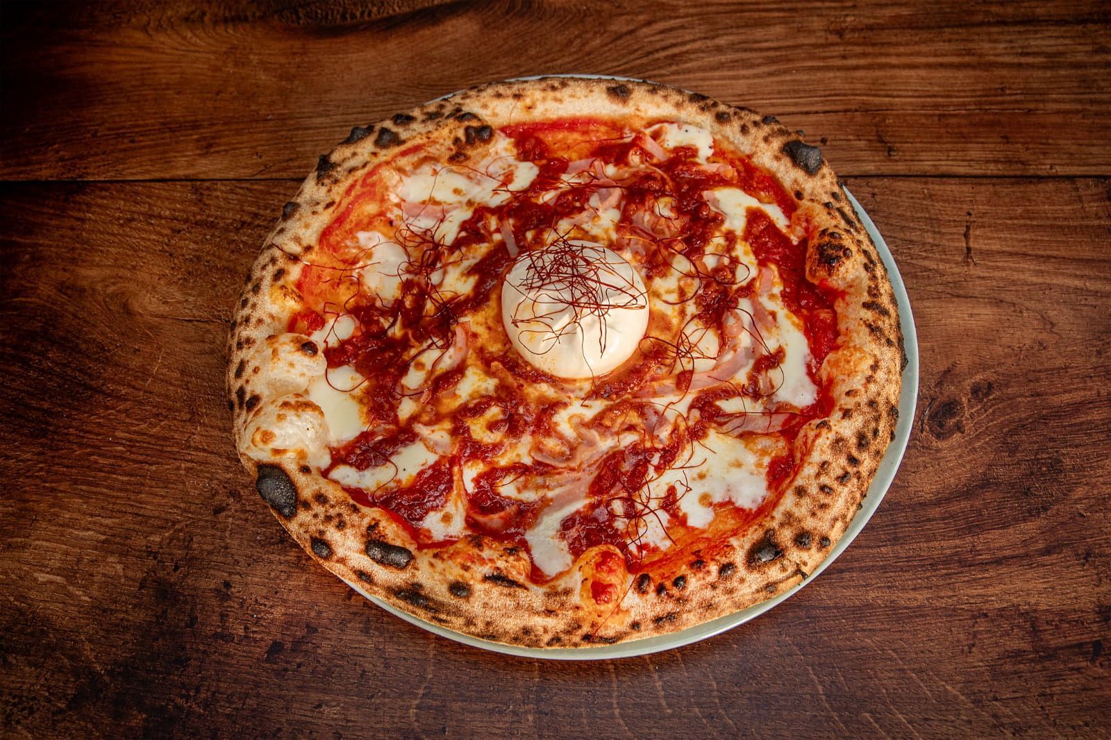 Pizza con masa, salsa, queso y un ingrediente central, en un plato, sobre una mesa de madera.