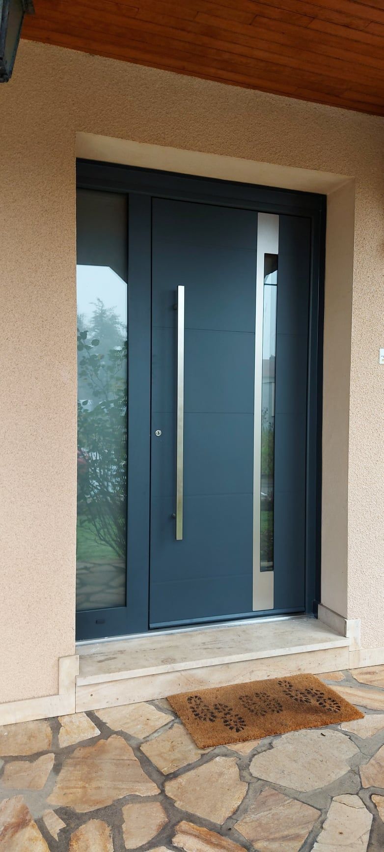 Porte d'entrée en aluminium de couleur gris anthracite avec poignée verticale et des vitres en longueurs opaques