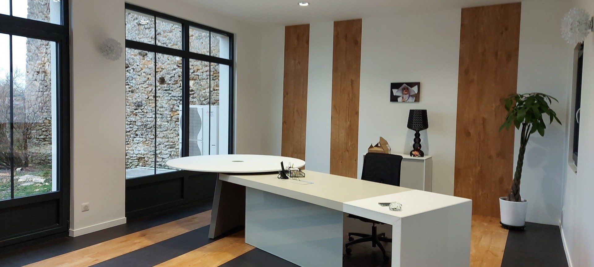 Intérieur d'un bureau de particulier avec table ovale à droite donnant sur une porte fenêtre noire