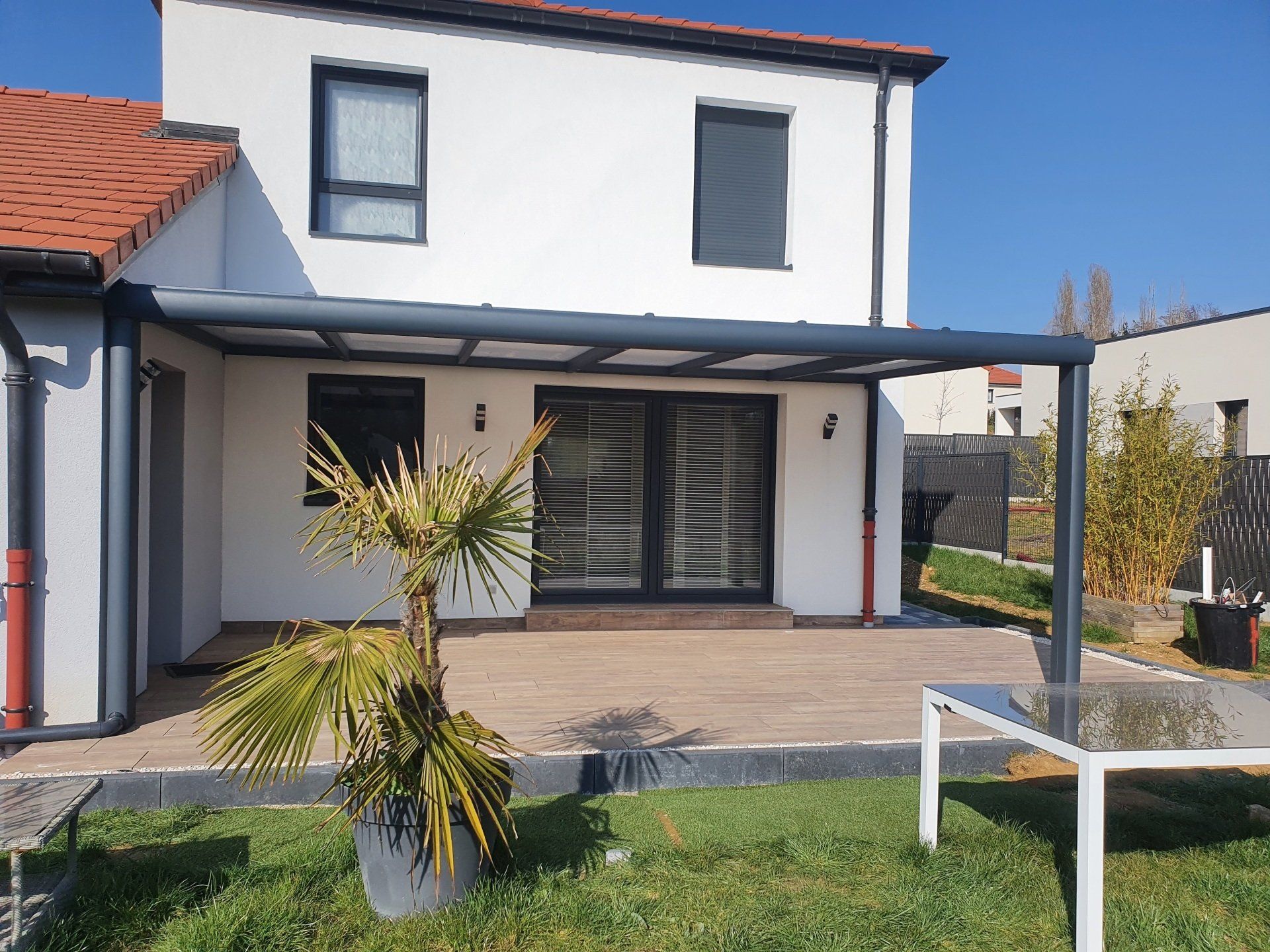 Pergola sombre devant une maison blanche à deux étages