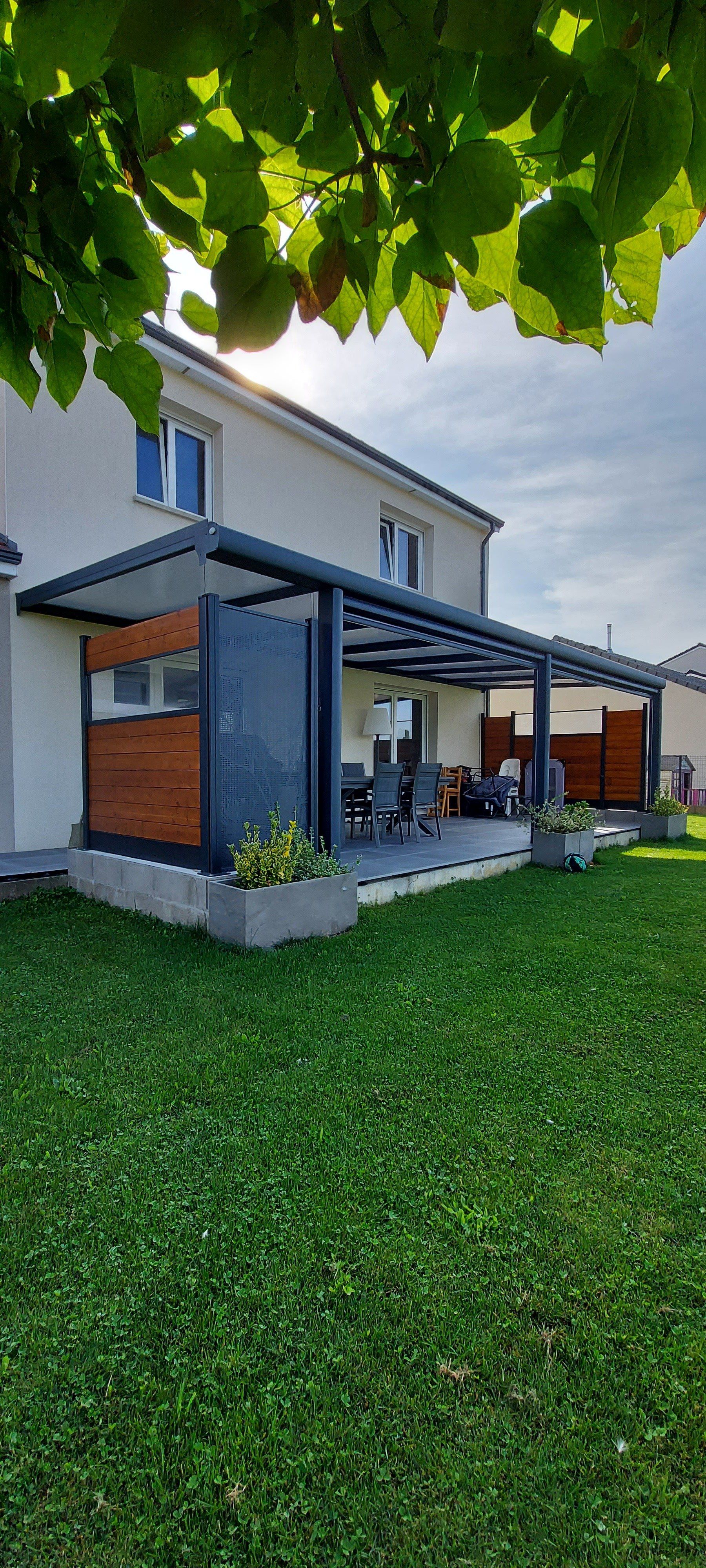 Pergola noire au-dessus d'une terrasse avec toit ouvrant en store banne, plus occultant sur les côtés