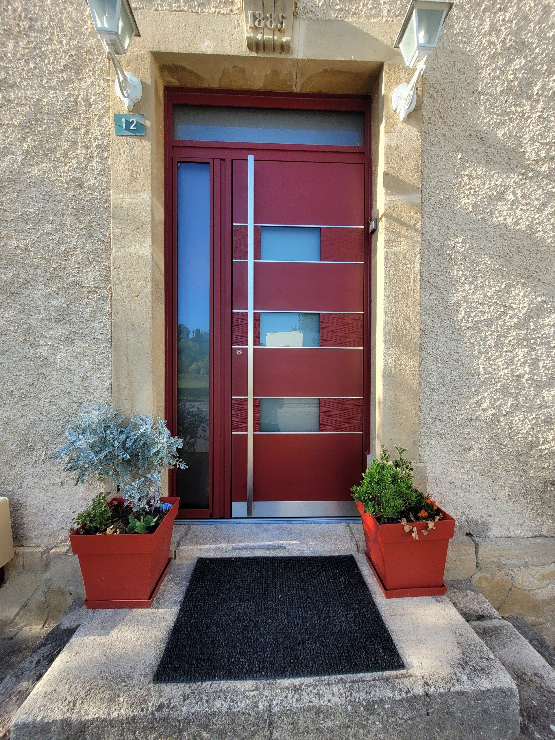Porte contemporaine rouge vif avec des lignes épurées et poignée en inox.
