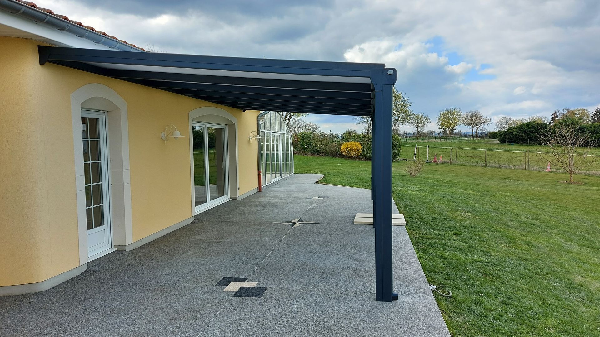 Pergola sur terrasse en carrelage avec maison de crépi jaune