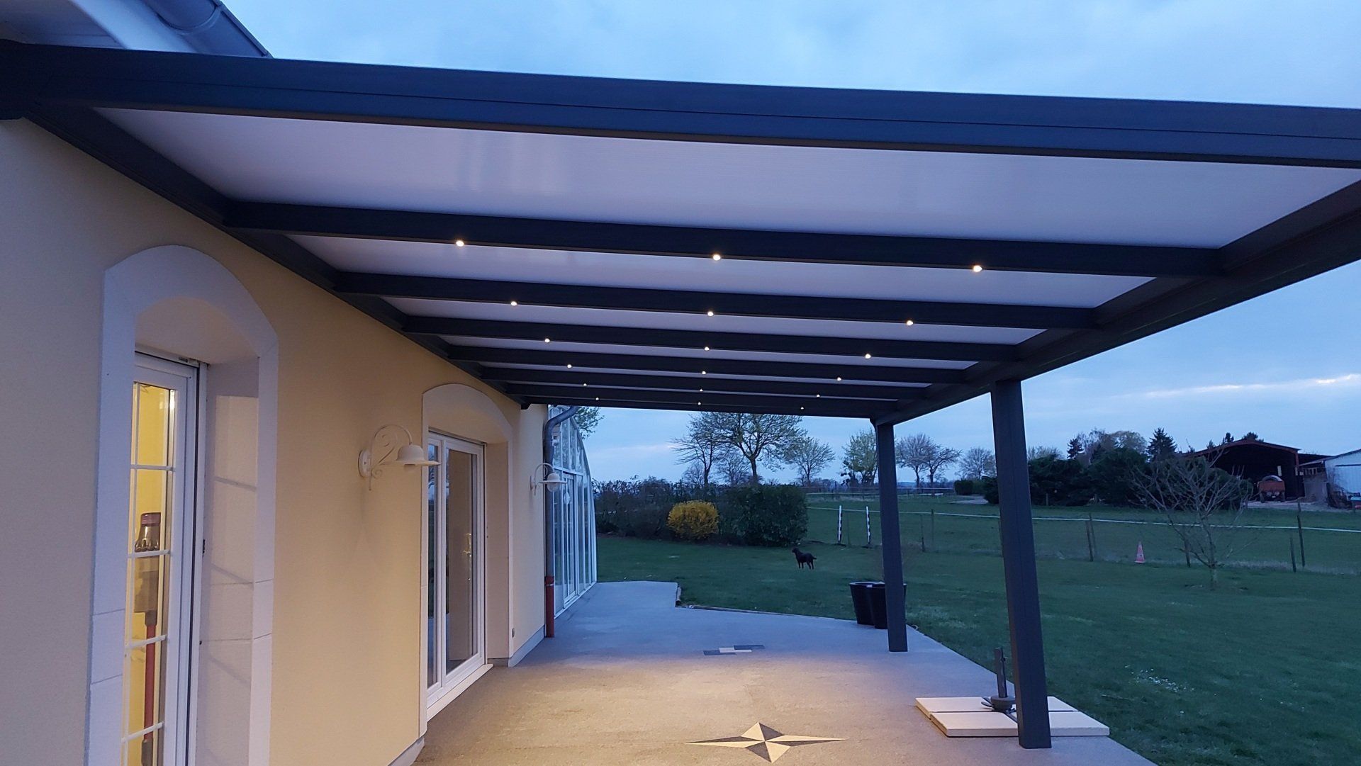 Pergola sombre en aluminium avec panneaux clairs protégeant une terrasse en béton