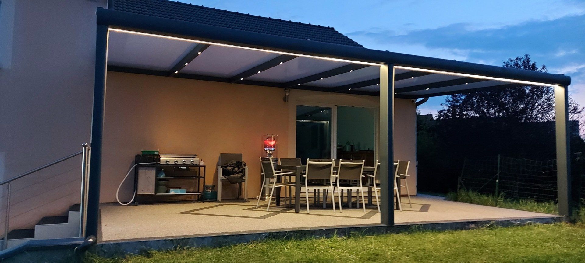 Pergola sombre disposant de luminaires pour éclairer une terrasse avec table et chaises