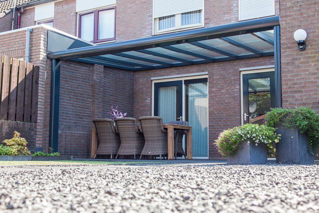 Pergola métallique sombre rattachée à trois pans d'une maison aux briques rouges