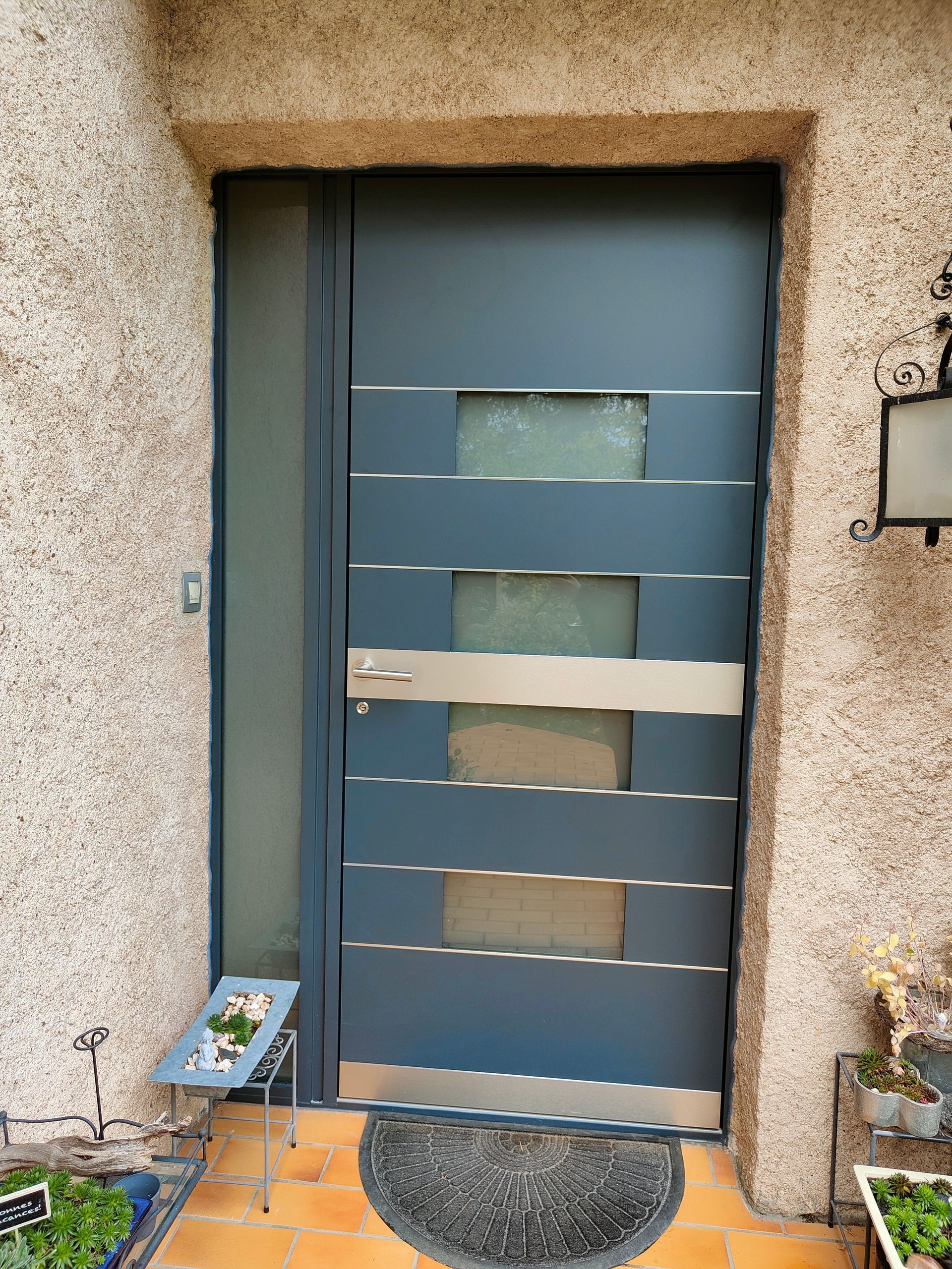 Porte d'entrée de couleur grise et poigné vertical en bois en son centre