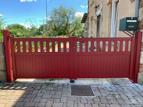 Portail coulissant rouge de forme simple avec des sortes de barreaux sur le haut