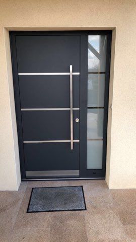 Porte moderne noire en acier avec une large poignée verticale et un design minimaliste.