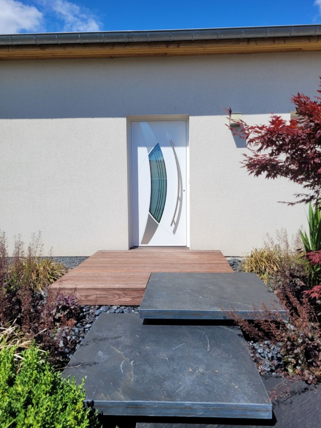 Porte d'entrée blanche vue de loin avec vitre en forme de feuille au milieu de la porte