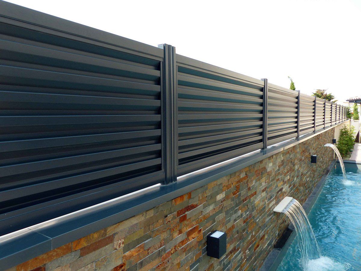 Clôture opaque métallique au dessus d'un muret en pierre bordan une piscine