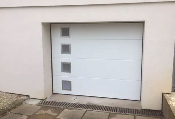 Porte de garage à bascule blanche avec des petits carreaux opaques sur le coté tout le long