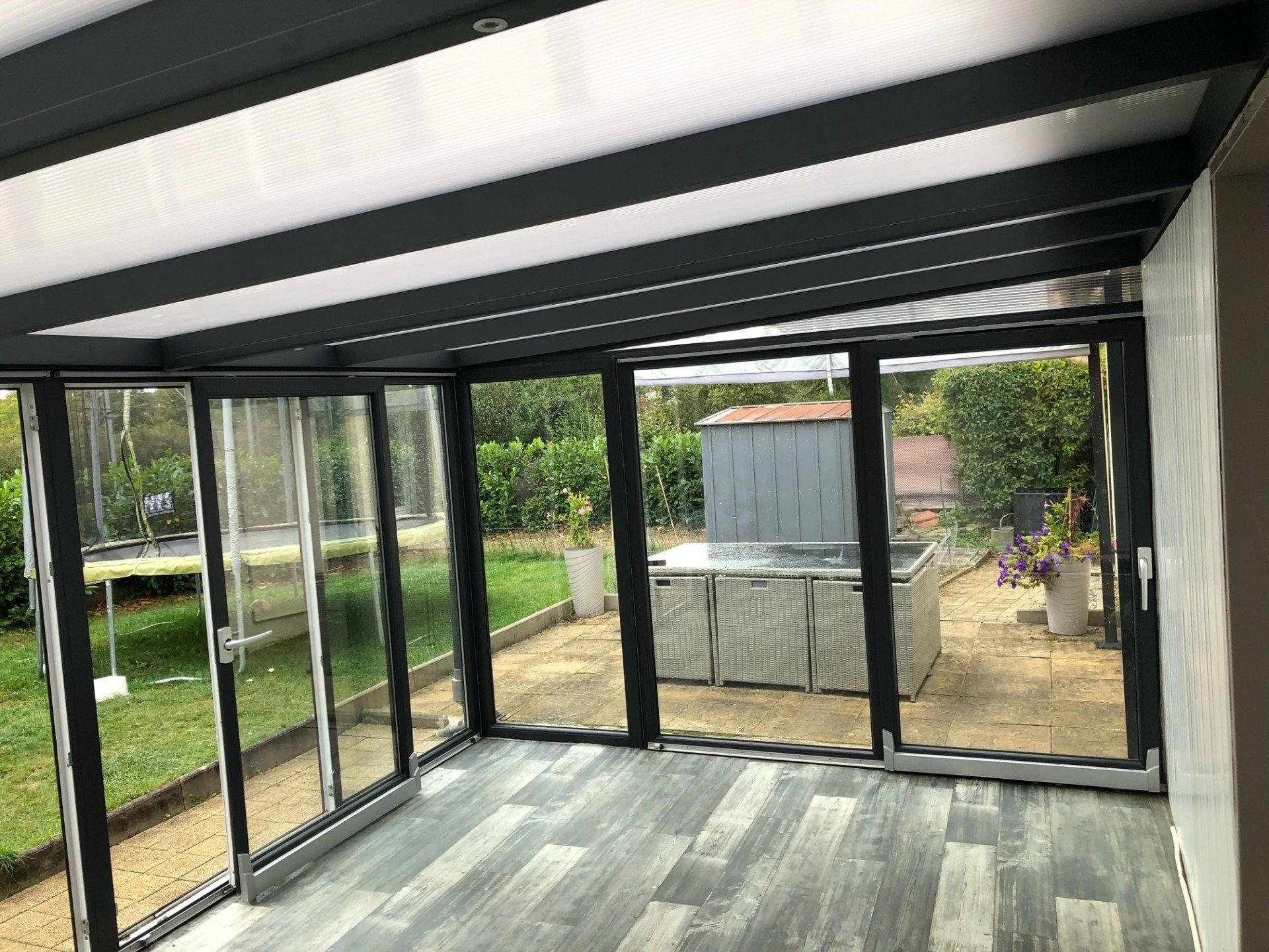 Pergola noire avec panneaux clairs et baie vitrée 