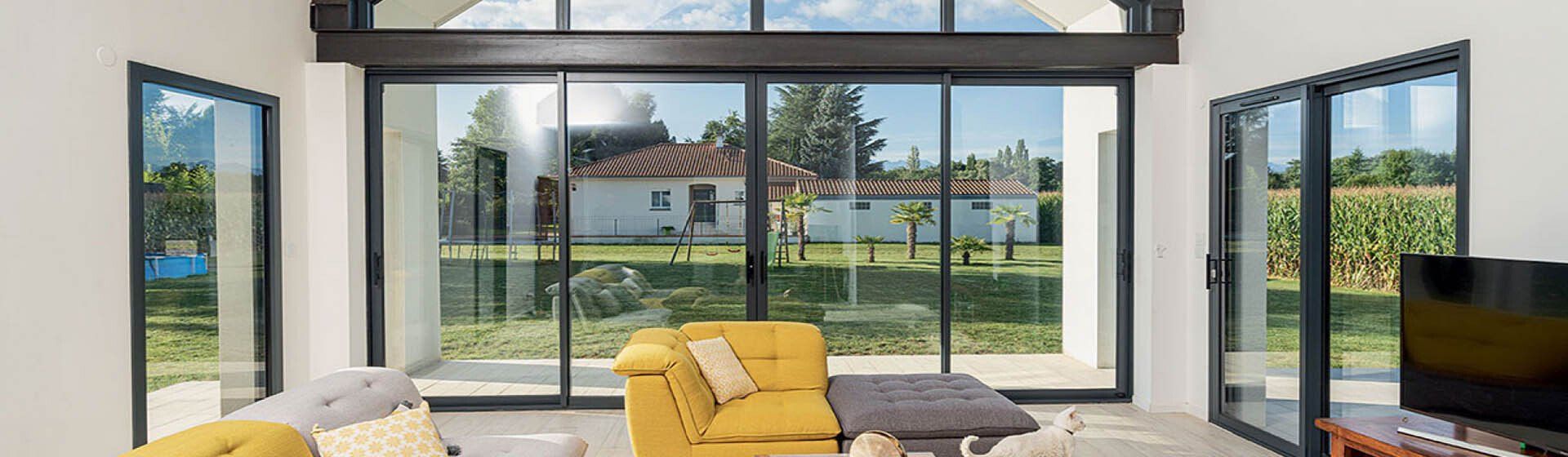 Grande baie vitrée sombre vue depuis le salon intérieur et donnant sur un jardin