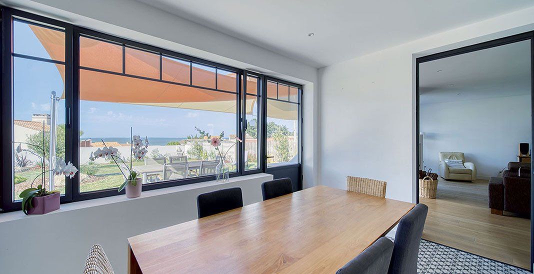 Salle à manger avec table en bois donnant sur une baie vitrée protégée par un store banne orange