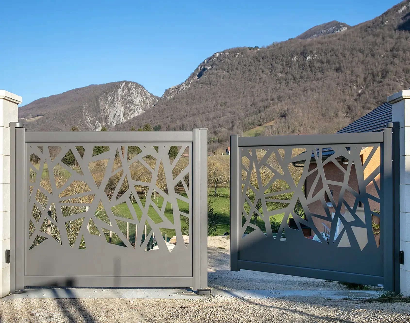 Portail battant de couleur grise avec formes artistiques et montagne en fond