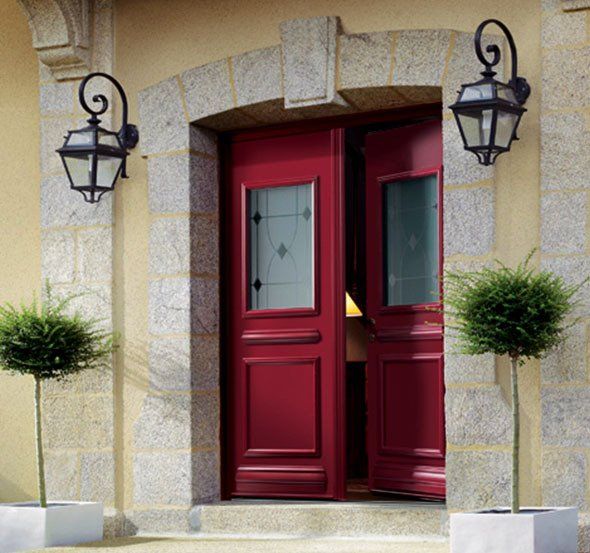 Grande porte d'entrée rouge encadrée dans une maçonnerie de bloc de marbre et deux luminaires de style victorien de chaque côté