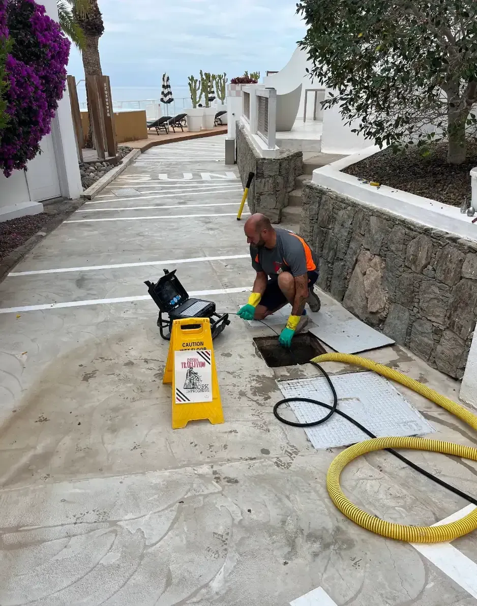 Hombre trabajando en un desagüe. Señal de precaución amarilla y equipo en un camino de hormigón, en una zona costera.