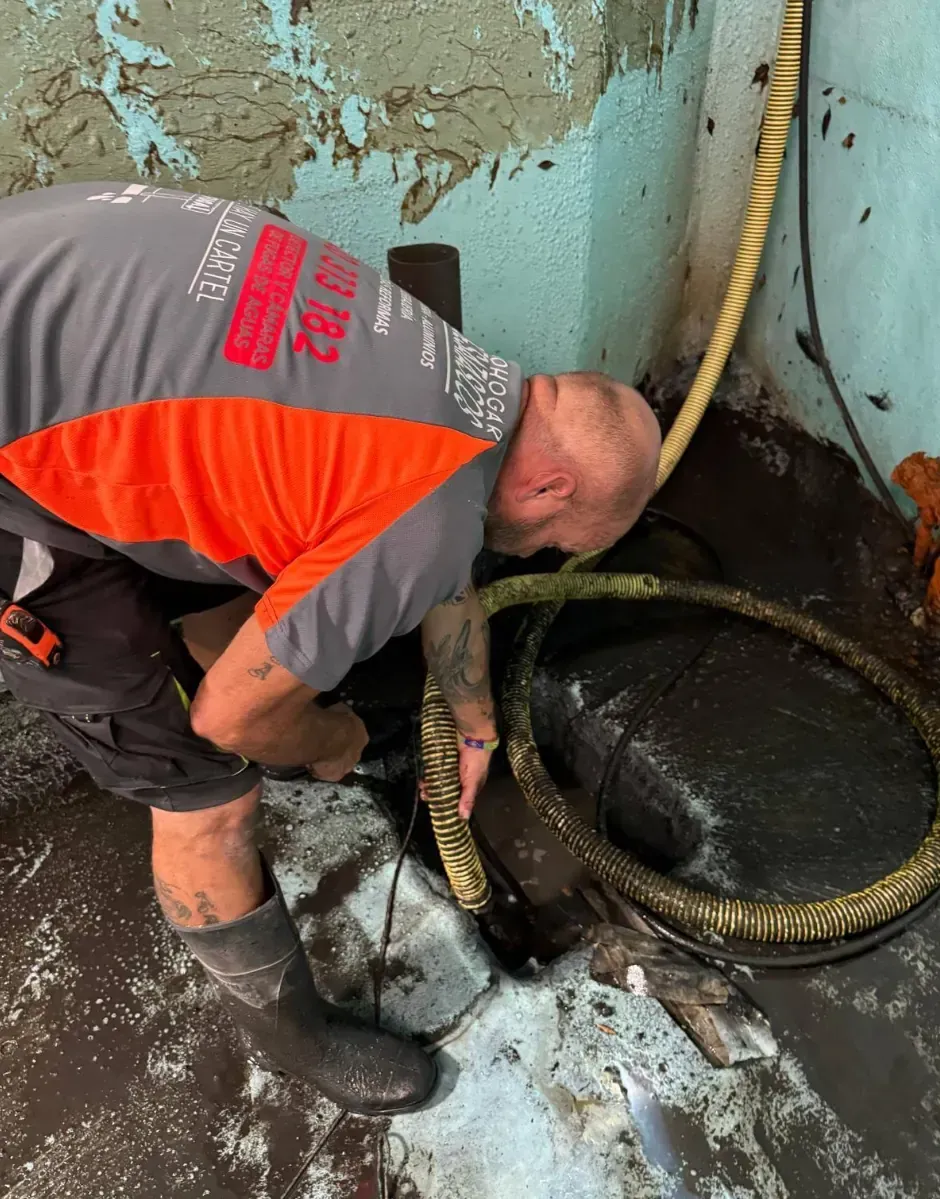 Hombre con ropa de trabajo trabajando cerca de una tubería oscura y aceitosa en un piso sucio.