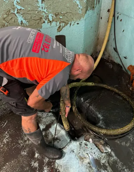 Hombre con ropa de trabajo trabajando cerca de una tubería oscura y aceitosa en un piso sucio.
