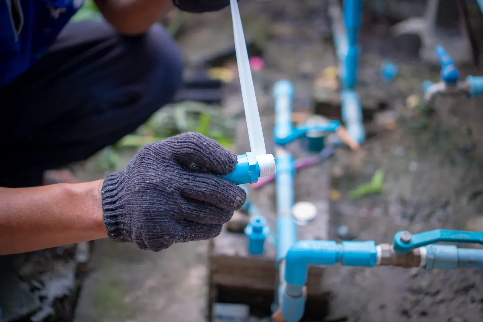 Persona con guantes negros conectando tuberías de PVC azules al aire libre.