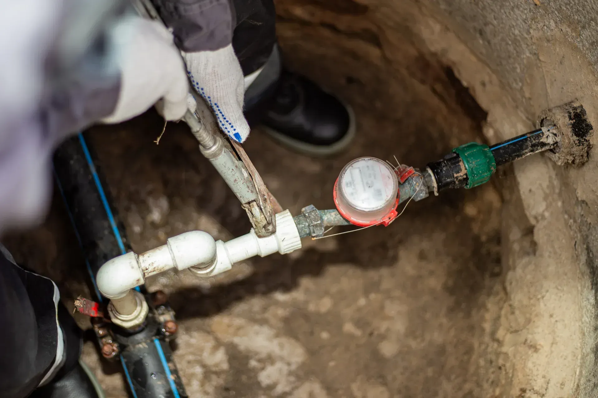 Persona con guantes repara un medidor de agua en un pozo de hormigón.
