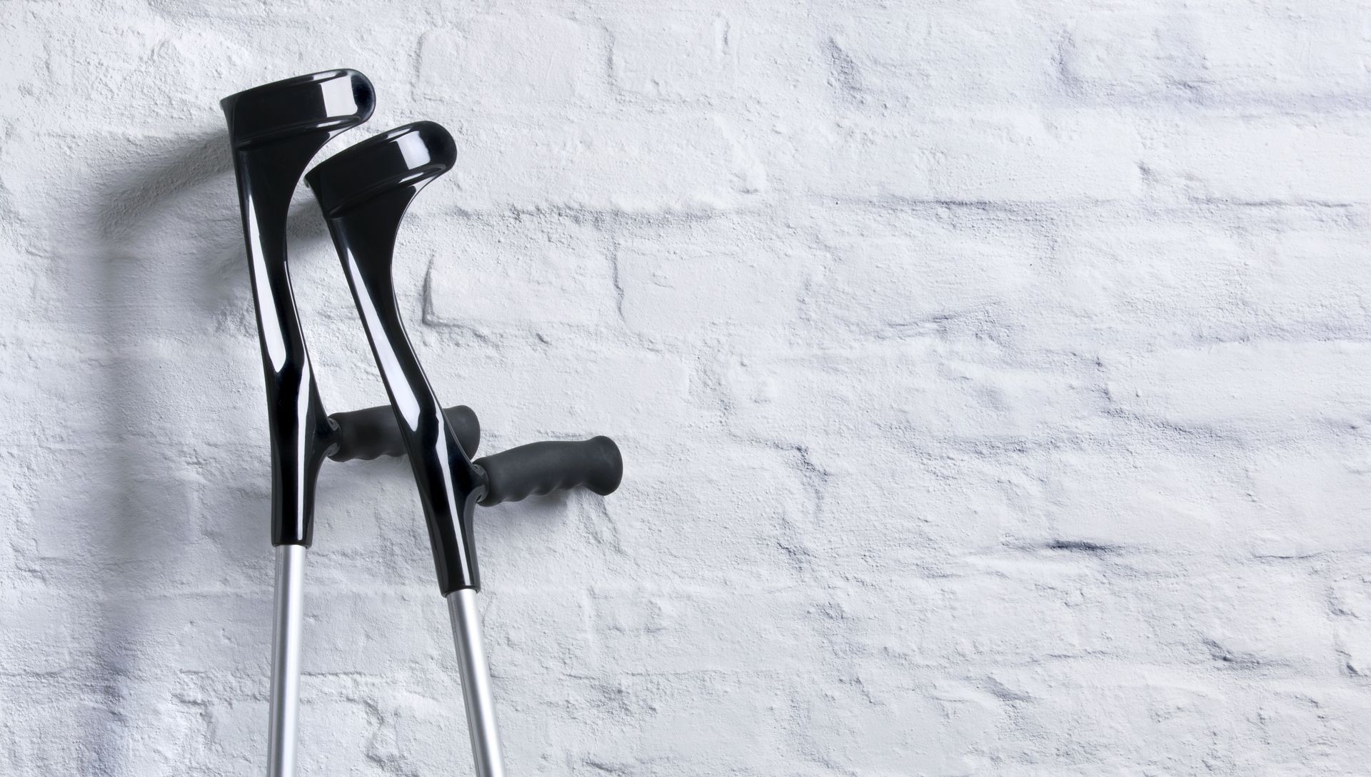 Une paire de béquilles noires appuyées contre un mur de briques blanches.