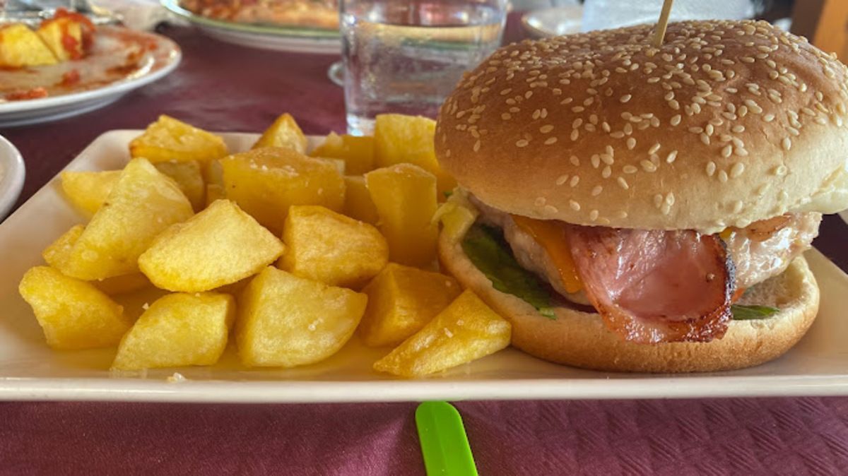 Una hamburguesa y papas fritas en un plato blanco sobre una mesa.