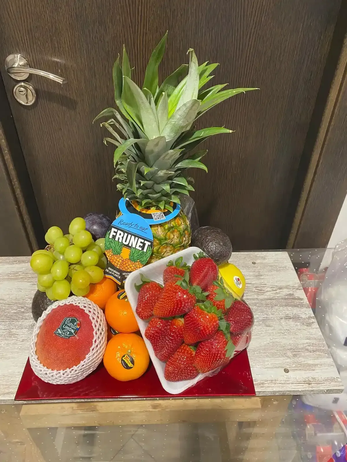 Exhibición de frutas con piña, uvas, naranjas, fresas, aguacate y fruta del dragón sobre una mesa.