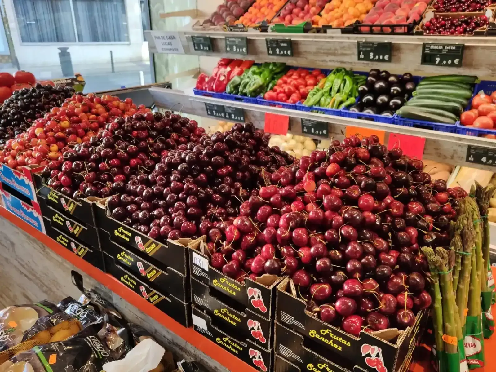 Puesto de frutas y verduras que exhibe cestas llenas de cerezas rojas y otras frutas coloridas en un mercado.