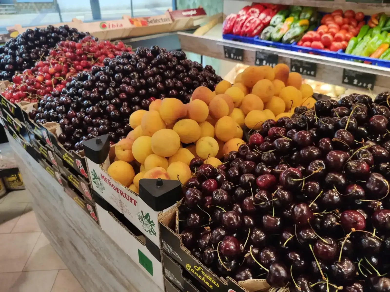 Exhibir frutas rojas, negras y amarillas en los pasillos de un supermercado.