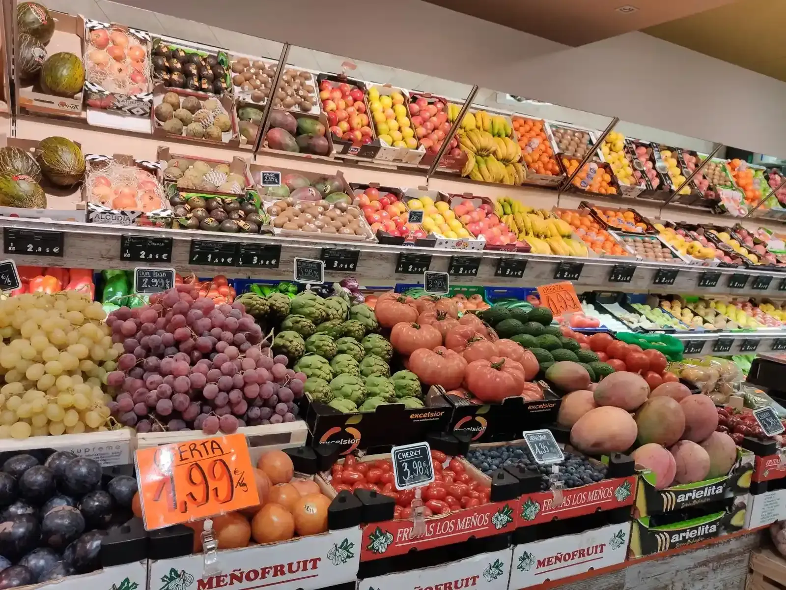 Exhibición de frutas y verduras frescas variadas en un supermercado, con coloridos contenedores apilados.