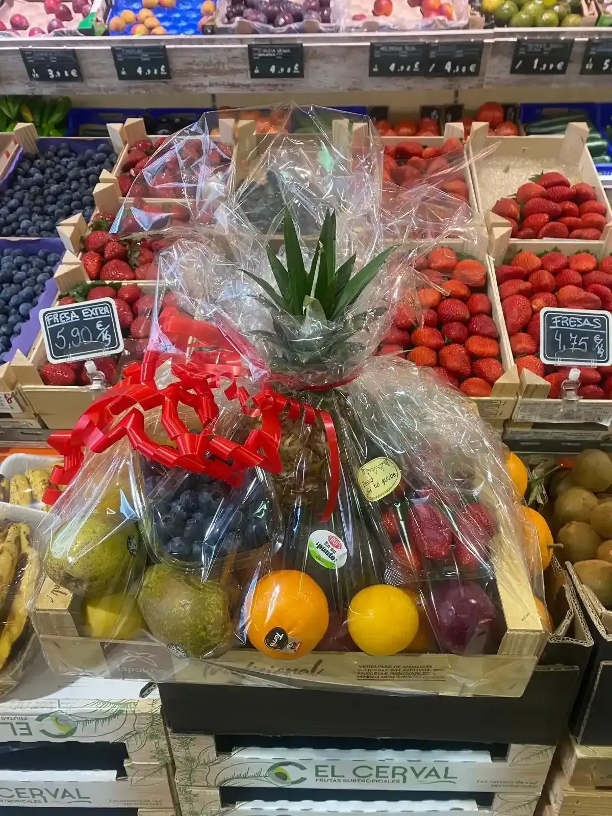 Cestas de fruta envueltas con fresas, plátanos, cítricos y un centro de mesa de piña en un puesto del mercado