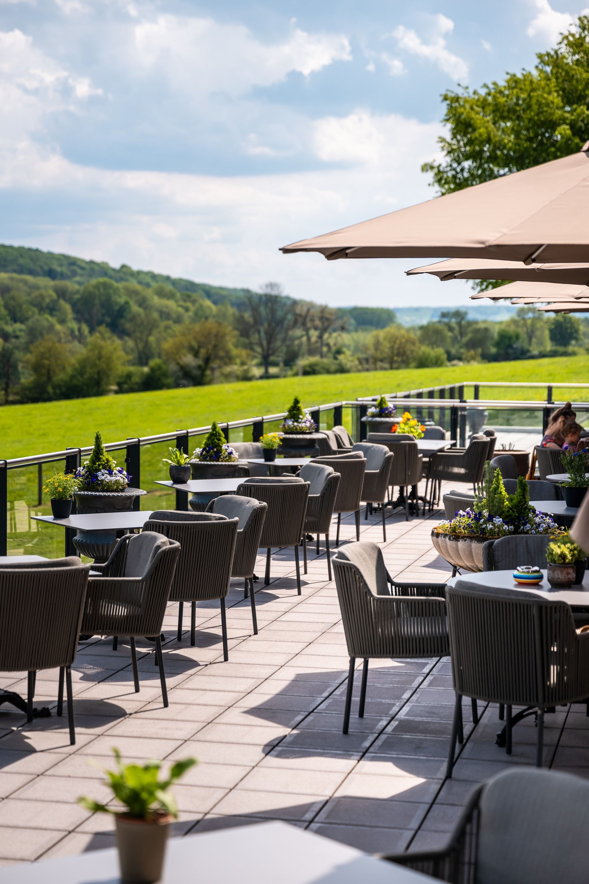 Een terras met tafels, stoelen en parasols met uitzicht op een veld.
