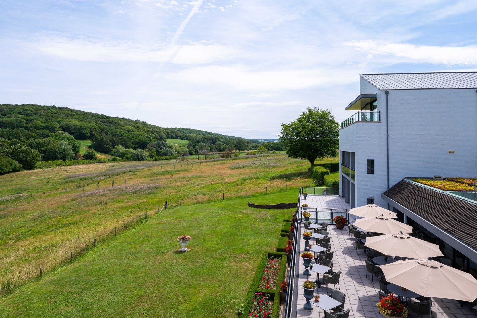 Een terras met tafels, stoelen en parasols met uitzicht op een veld.
