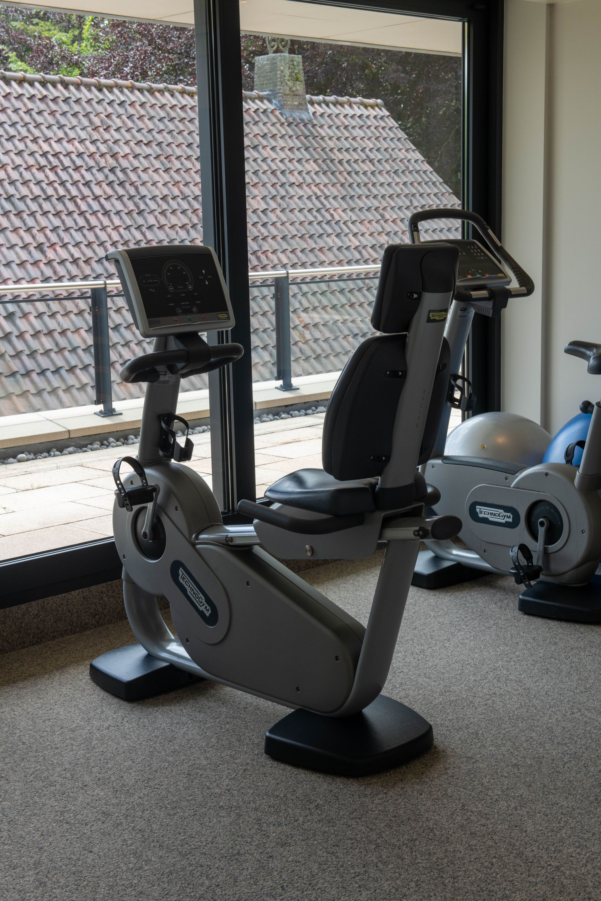 Een ligfiets staat in een sportschool naast een raam.