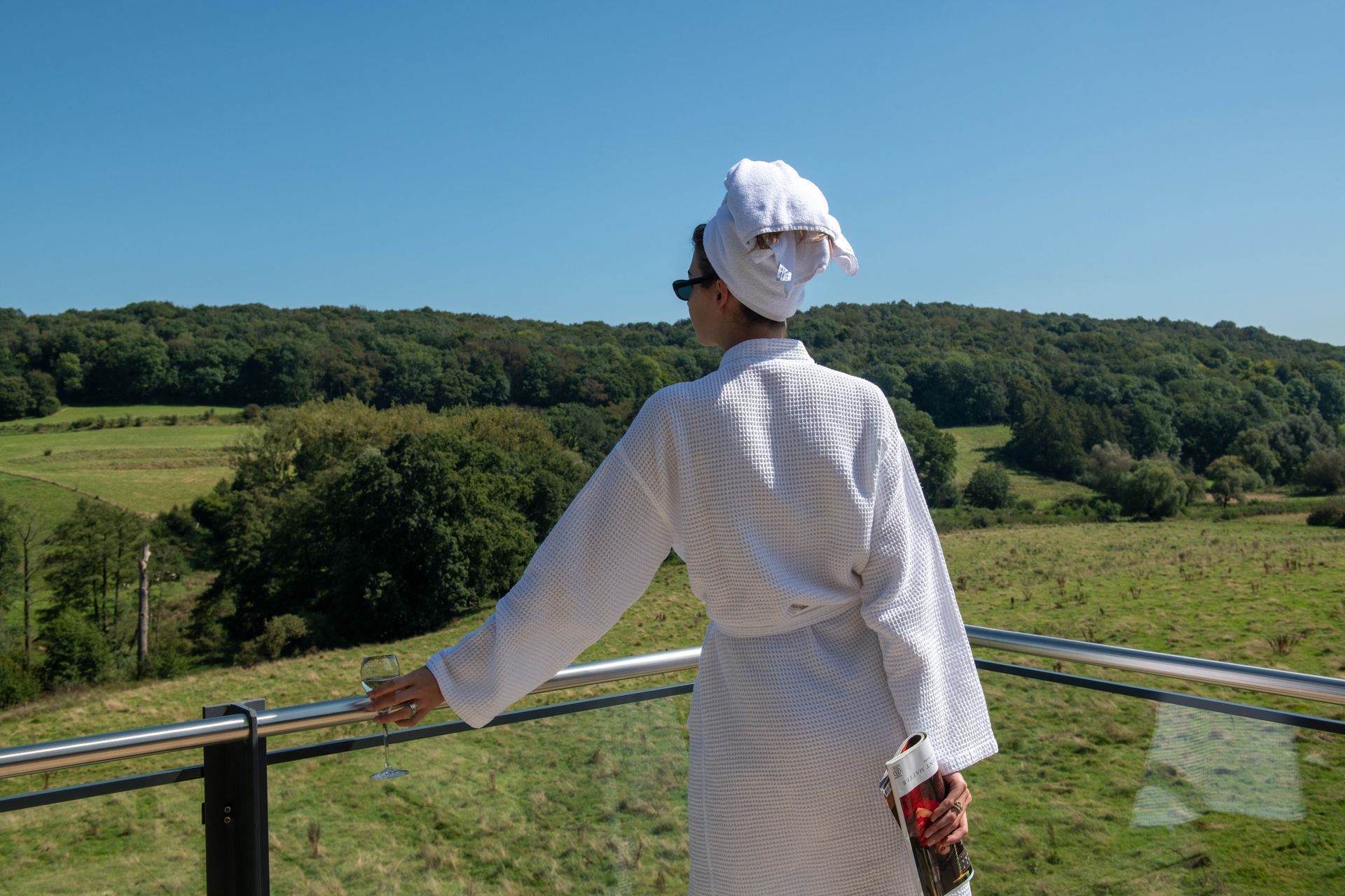 Een vrouw in een badjas staat op een balkon met uitzicht op een veld.