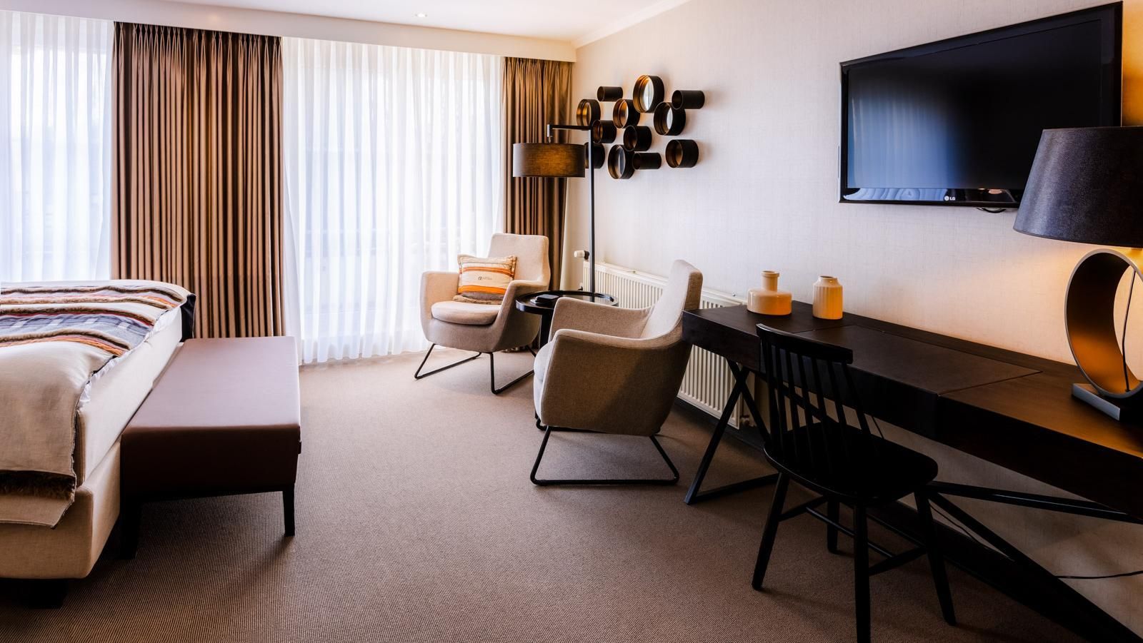 Een hotelkamer met een bed, stoelen, bureau en televisie.