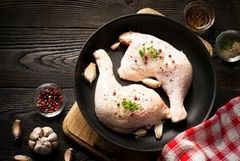 Présentation d'un poulet sur une planche en ardoise avec des tomates cerises et de l'oignon rouge.