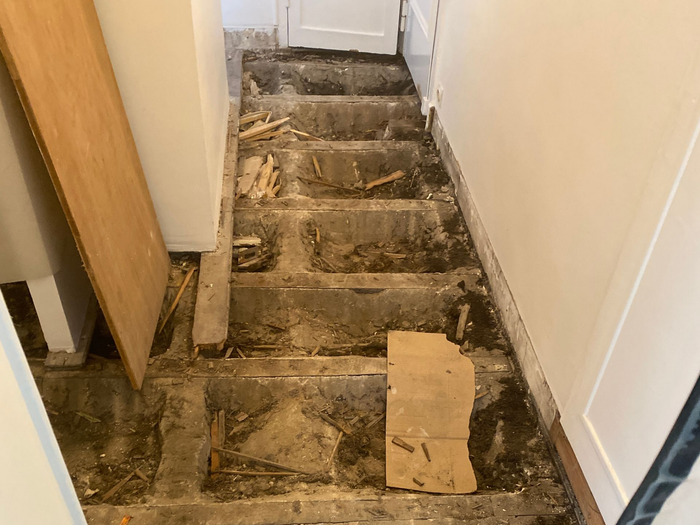 Escalier intérieur endommagé, charpente apparente et débris.