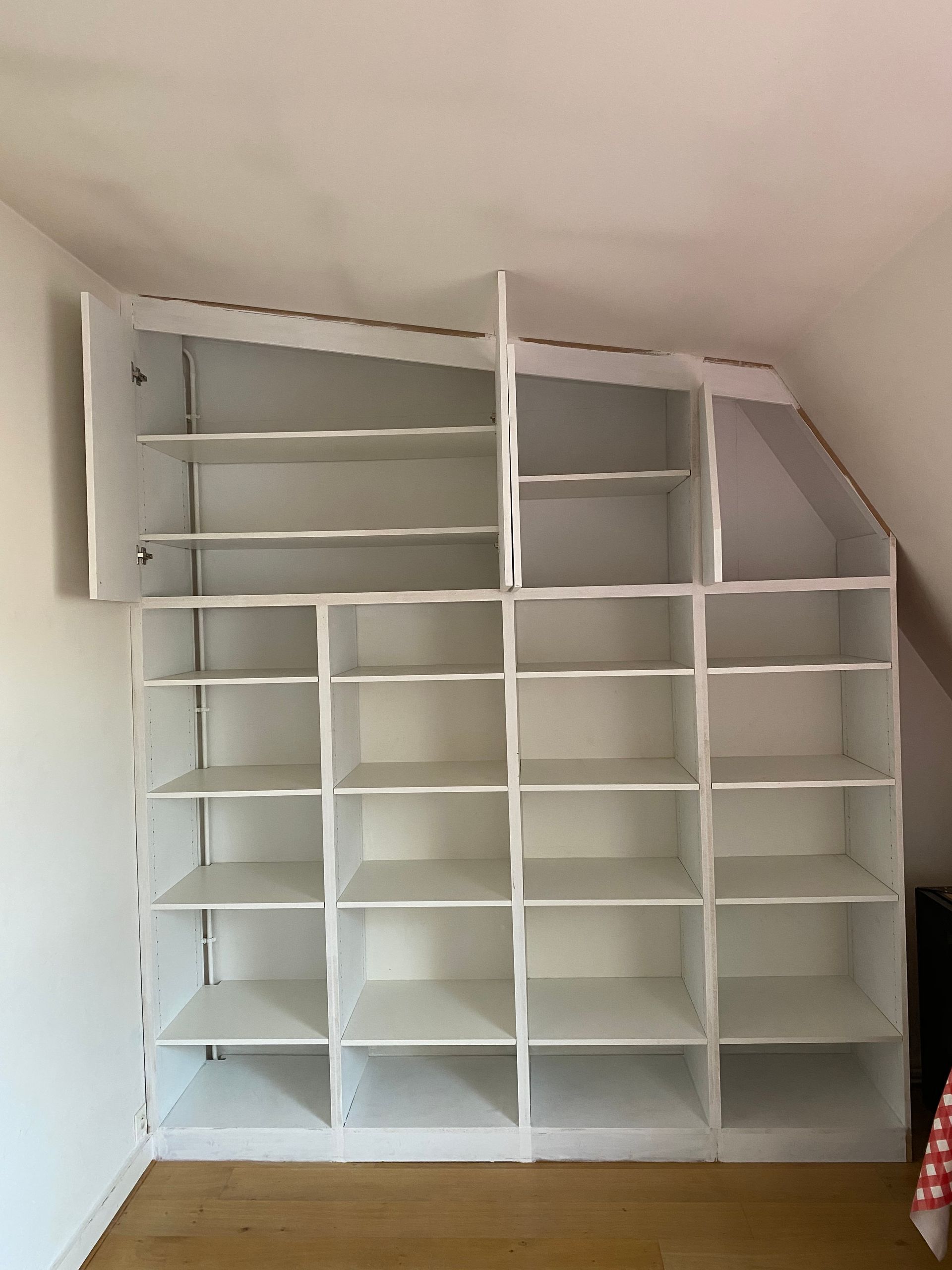 Étagère encastrée blanche avec plusieurs compartiments vides dans une pièce au plafond mansardé.