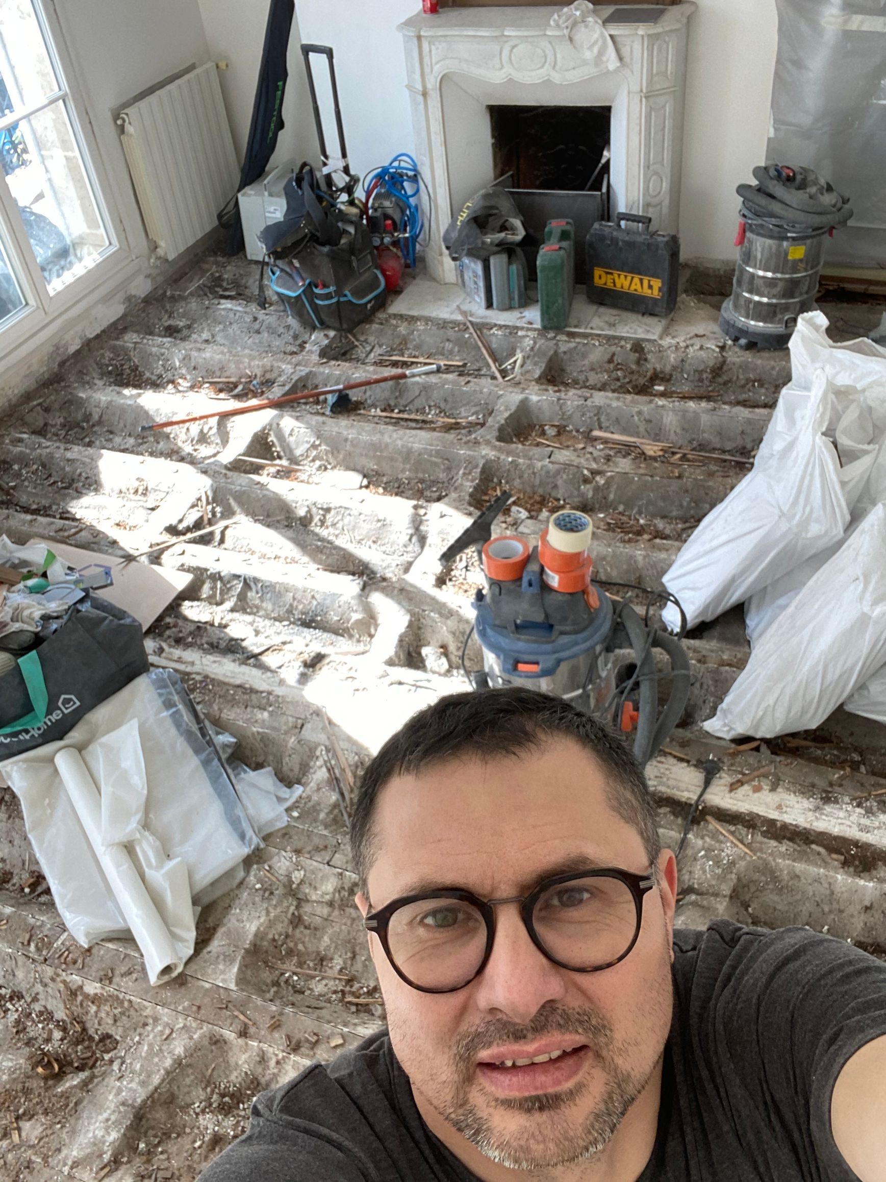 Un homme prend un selfie dans une pièce en désordre avec une cheminée, des outils et des matériaux de rénovation.