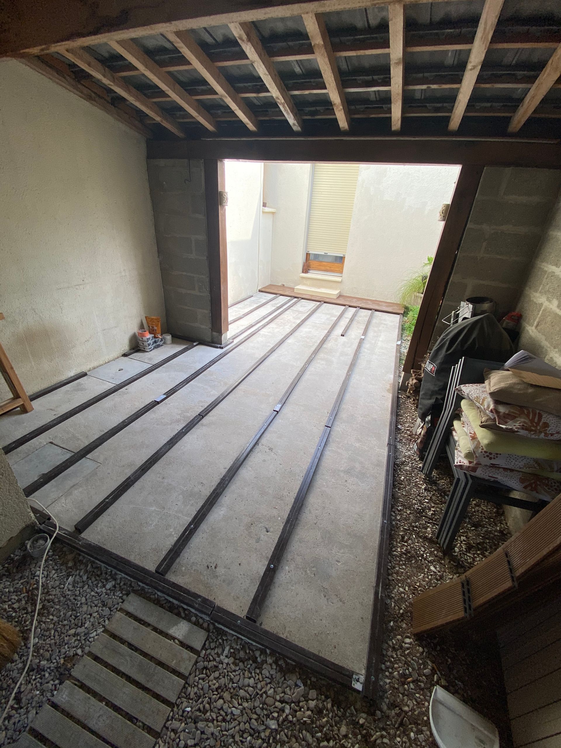 Pièce nue en cours de rénovation, avec solives de plafond et de plancher apparentes, porte ouverte sur un extérieur.