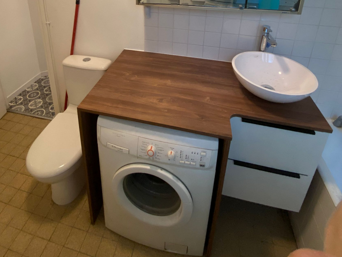 Petit meuble-lavabo de salle de bains avec une machine à laver sous un plan de travail en bois et un lavabo rond.