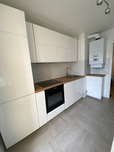 Cuisine moderne blanche avec plan de travail en bois, four encastré, évier et chaudière murale.