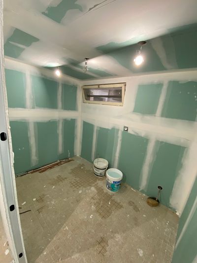 Salle de bains inachevée avec des cloisons sèches vertes, un sol carrelé, une fenêtre.