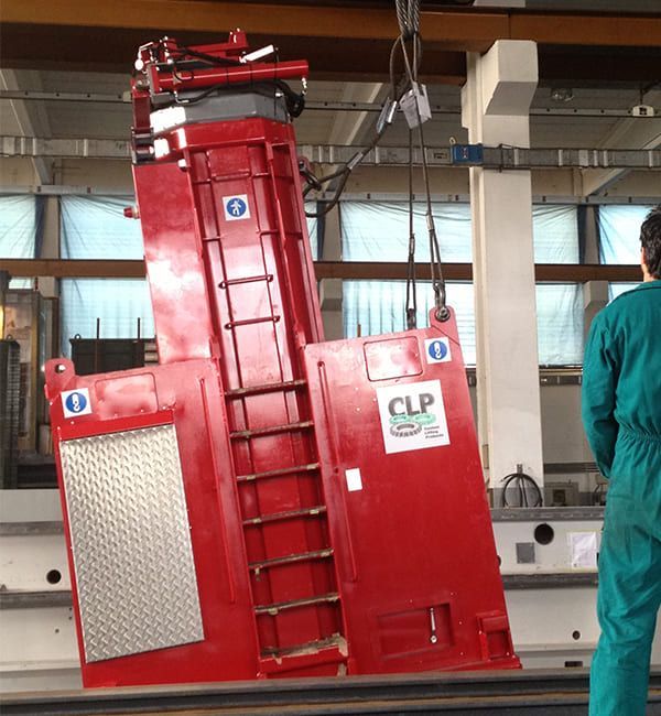 Machine industrielle rouge hissée dans une usine, un ouvrier observe.