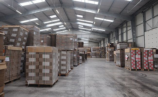 Intérieur d'entrepôt avec des piles de marchandises emballées sur palettes. Éclairage zénithal, sol en béton.